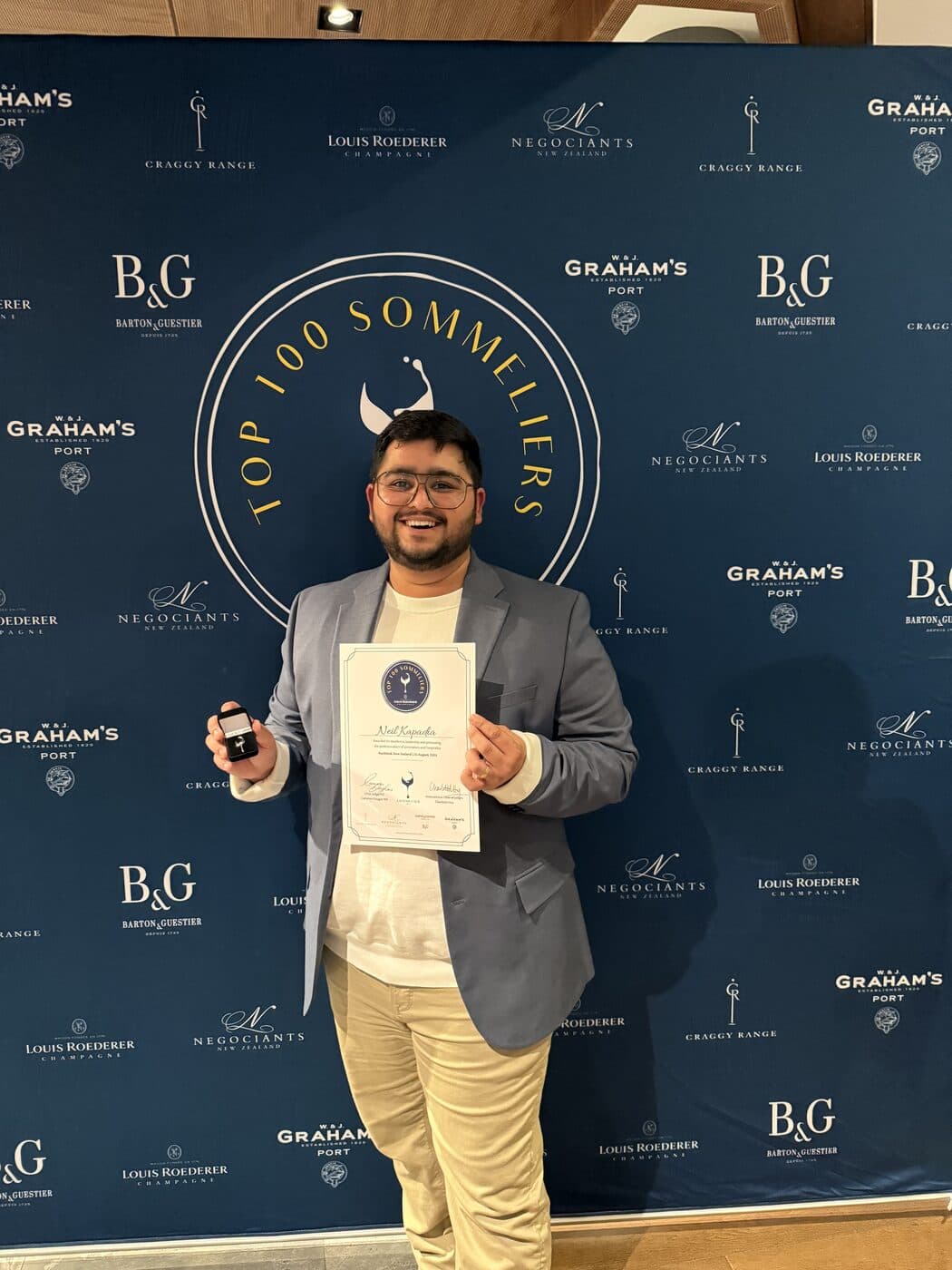 Neil Kapadia holding his New Zealand Top 100 Sommeliers certificate